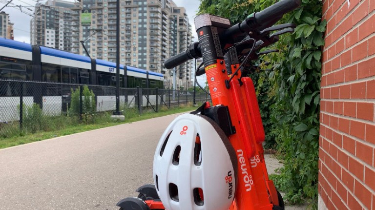 An orange e-scooter parked beside the ION LRT tracks in Waterloo Region.