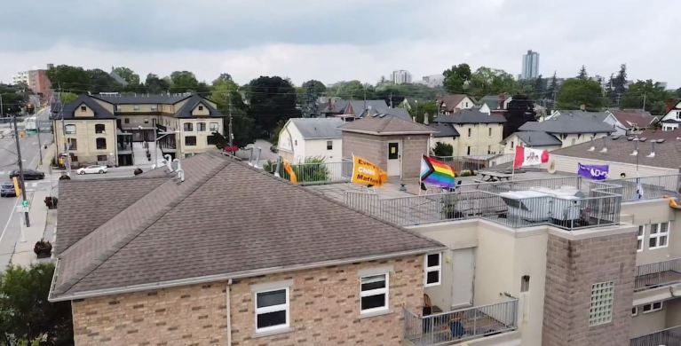 Aerial view of a multi-unit building with "Every Child Matters," Pride and other flags flying from the roof.