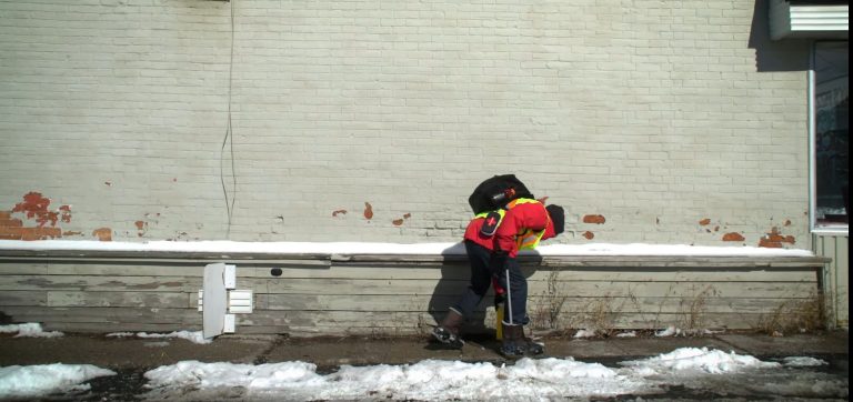 A man working for the WINS Program picks up discarded needles from a sidewalk.