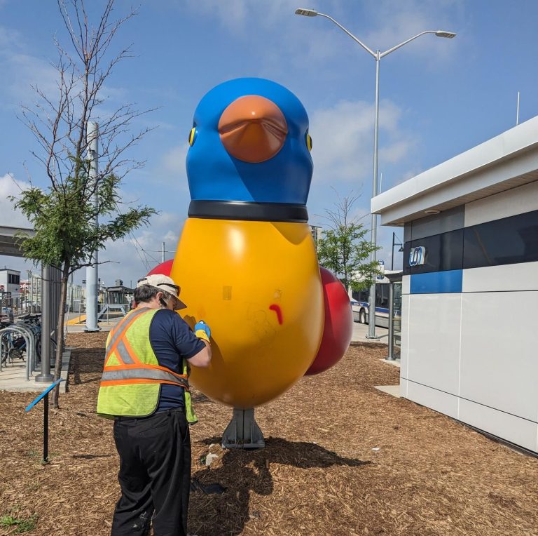 A worker cleans the colourful bird sculpture called "shaping Residency," located at the Fairway ION station.