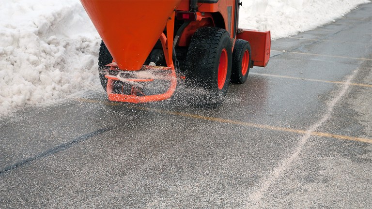 Salt being spread on pavement in a snowy parking lot.