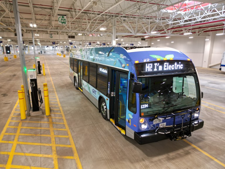 A shiny, new, blue electric bus parked inside a GRT facility.