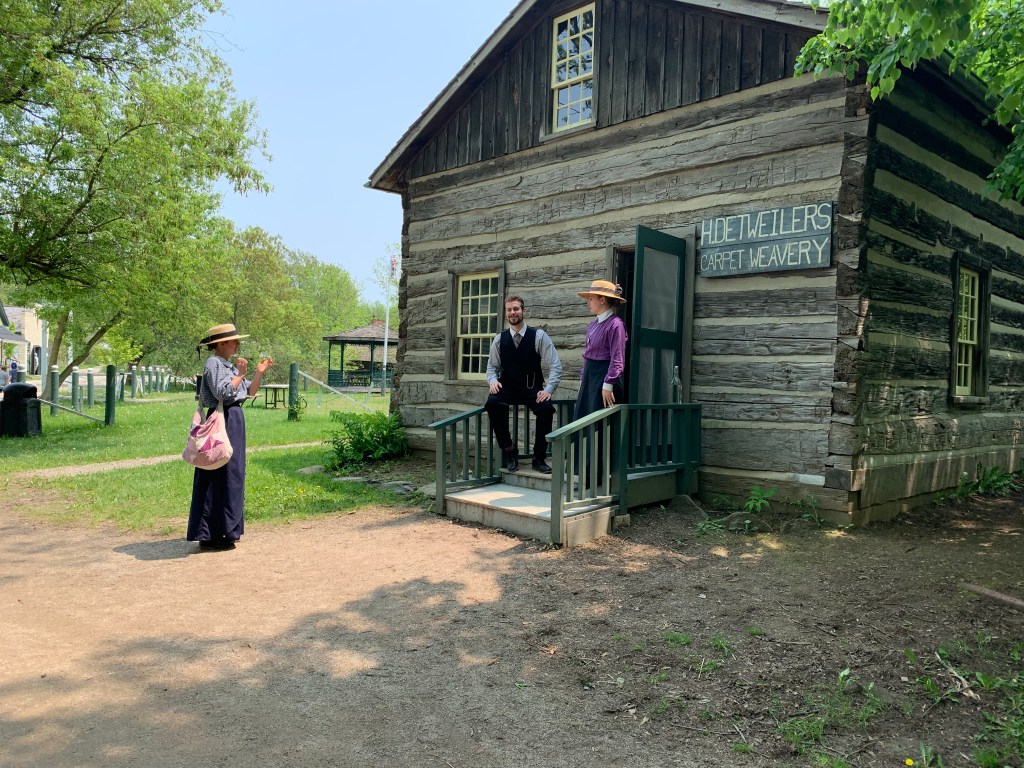 Staff in historical costumer stand outside the old buildings at Doon Heritage Village.