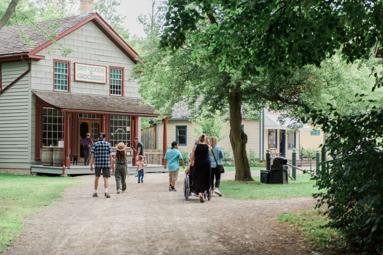 Visitors and staff in historical costumer walk outside the old buildings at Doon Heritage Village.