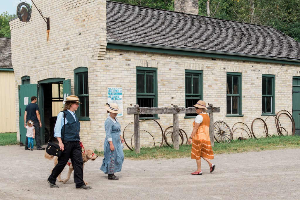 Visitors and staff in historical costumer walk outside the old buildings at Doon Heritage Village.