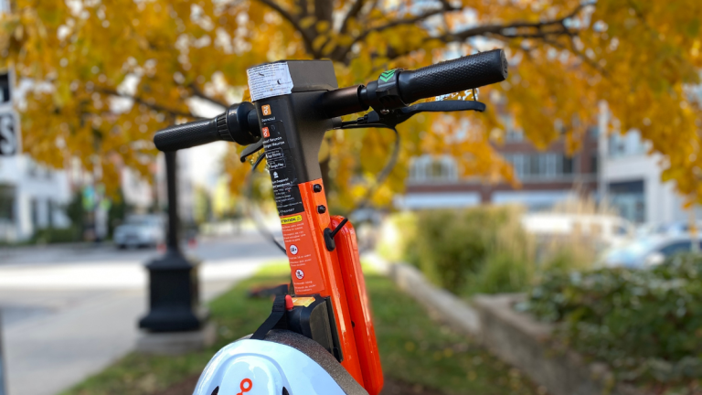 Handlebars and helmet on an orange Neuron e-scooter.
