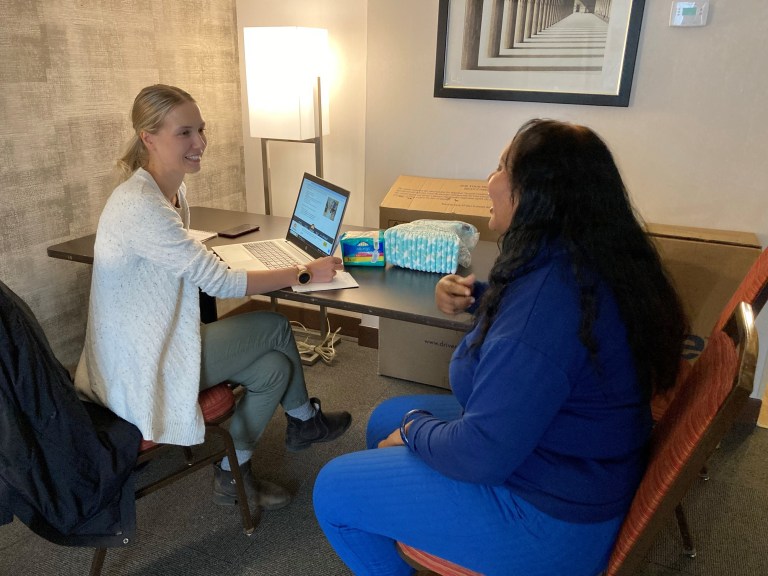 A woman talks with a nurse, seated at a table.