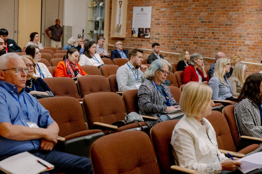 Attendees in theatre seating watch the Homes for All Summit.