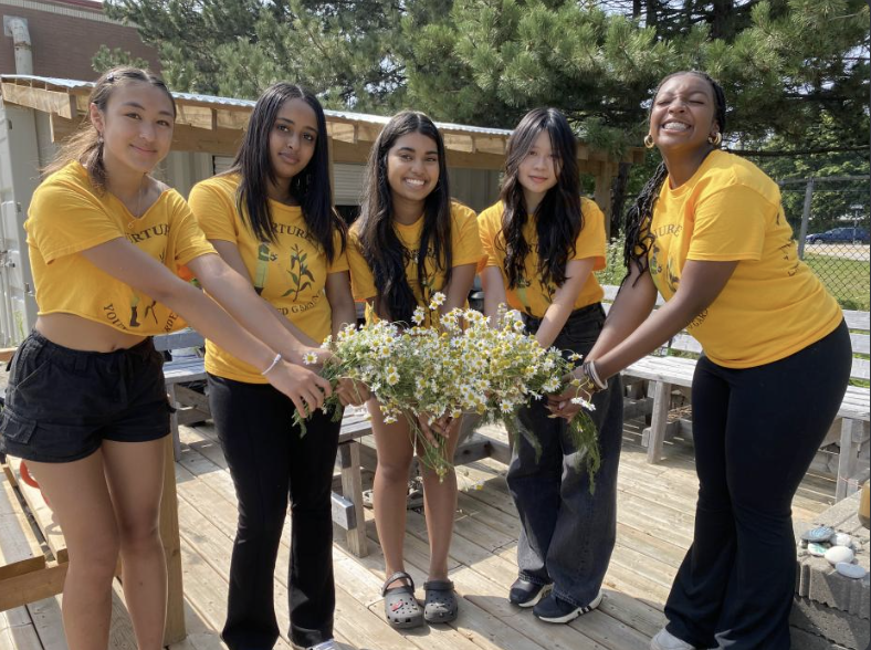 Five students in matching yellow t-shirts show off flowers from their gardens