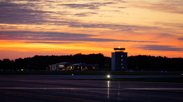 Region of Waterloo International Airport's runway and control tower with a bright orange sky behind.