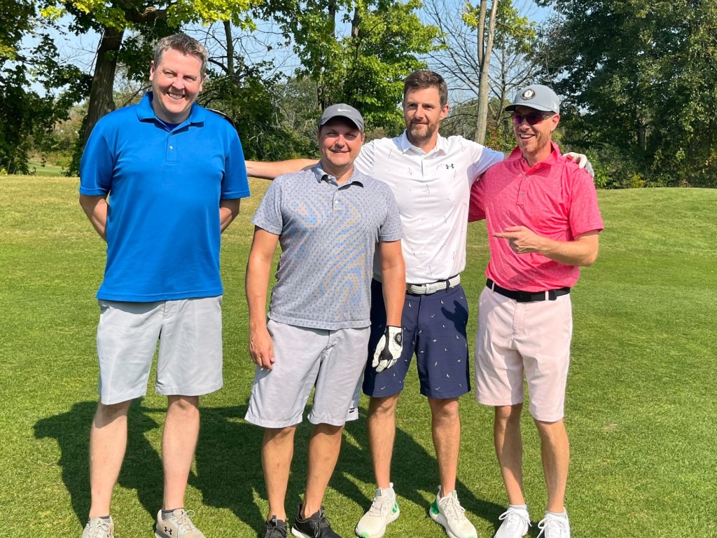 Four golfers stand on the course