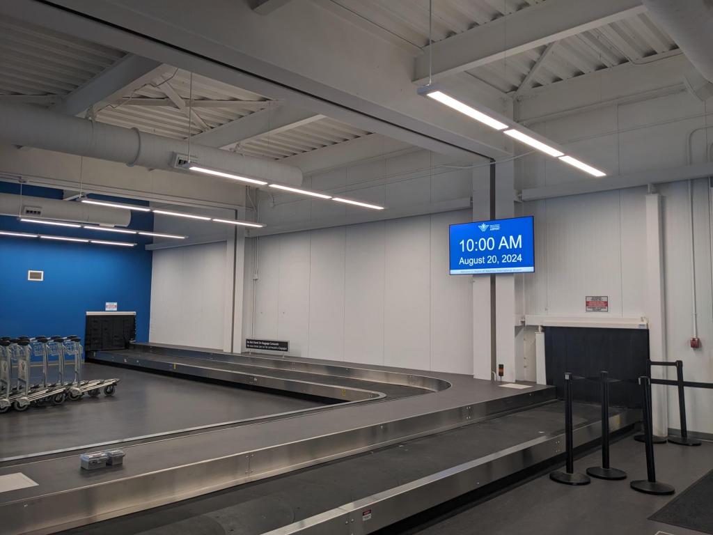 A plain white wall in the airport, with a baggage carousel in the foreground.