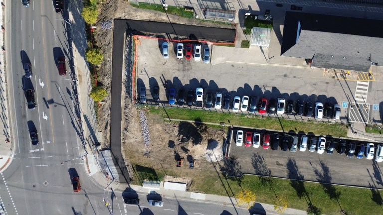 An aerial photo of a paved path beside a train station near a busy intersection.