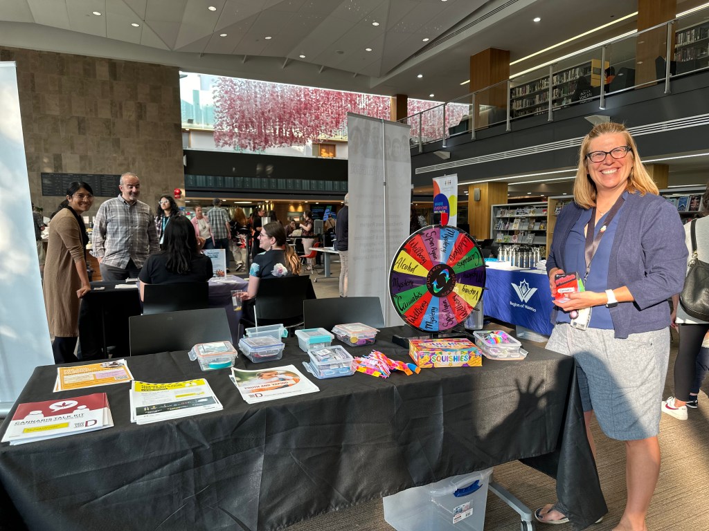 A woman stands near a table at the the “Newcomer Information Night: Health and Wellbeing Fair.”