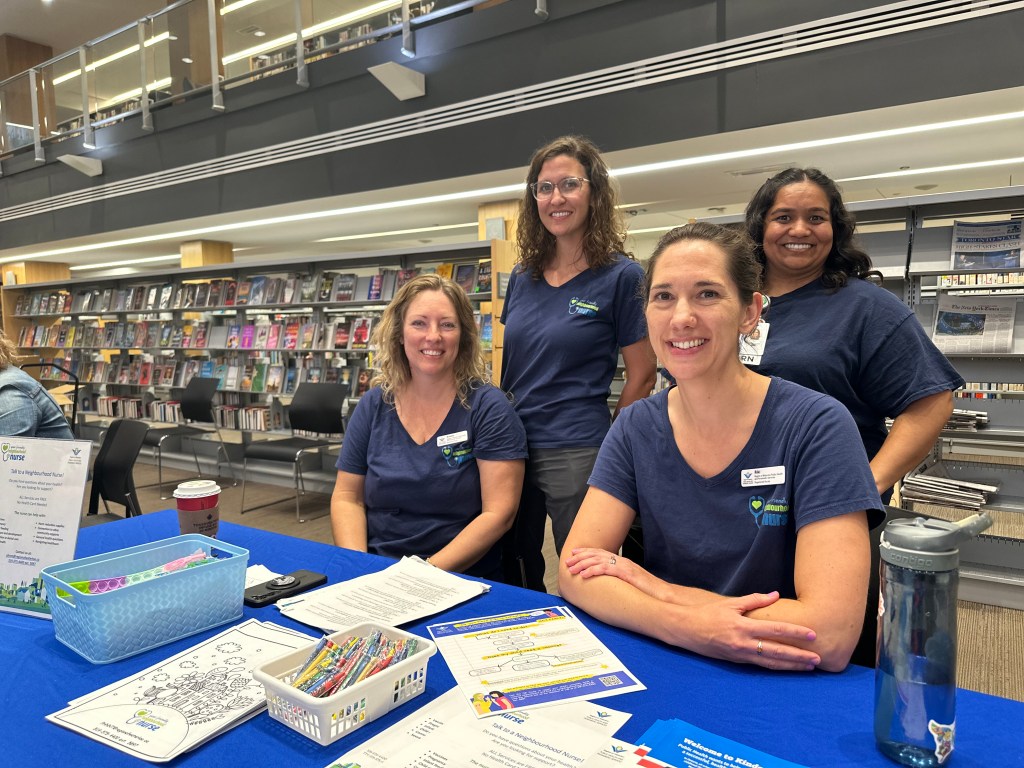 Four Public Health nurses sit at a table to welcome people at an educational event.