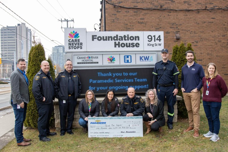 A group of 10 paramedics pose near a Grand River Hospital Foundation sign with their large donation cheque.