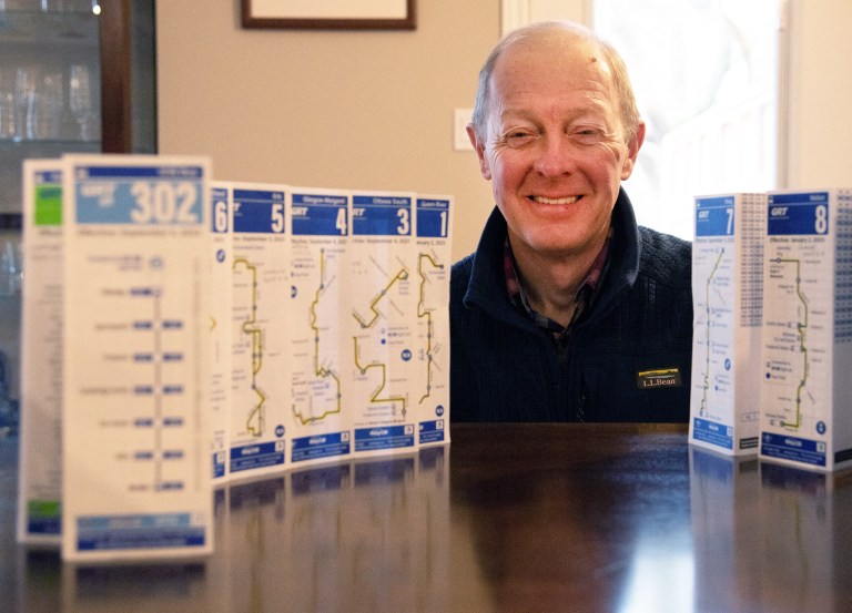 A man smiles with a series of paper bus schedules on a table.