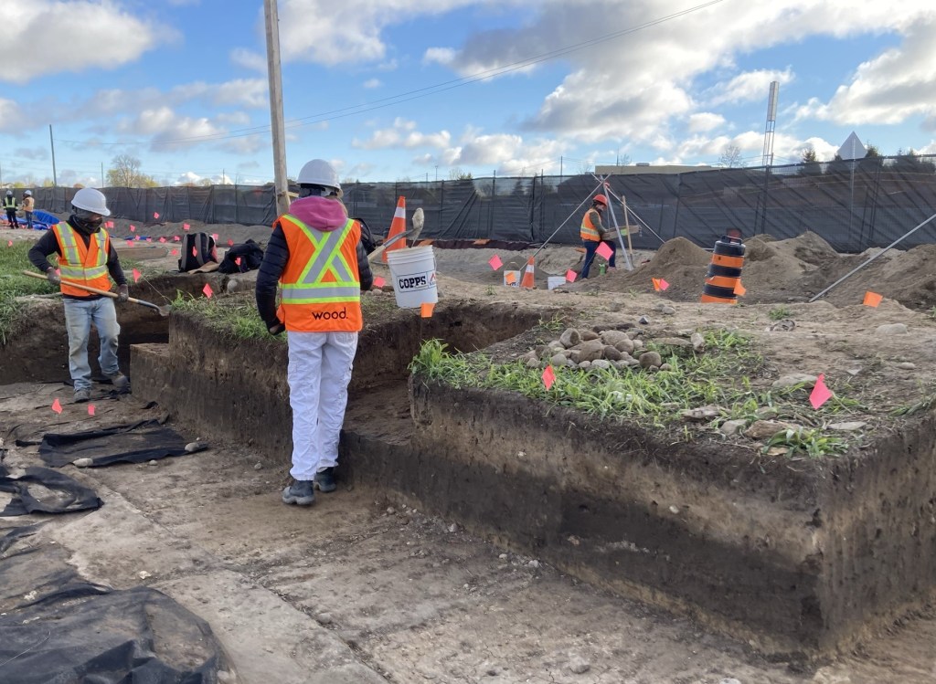 Group of people wearing vests and hard hats work outside.