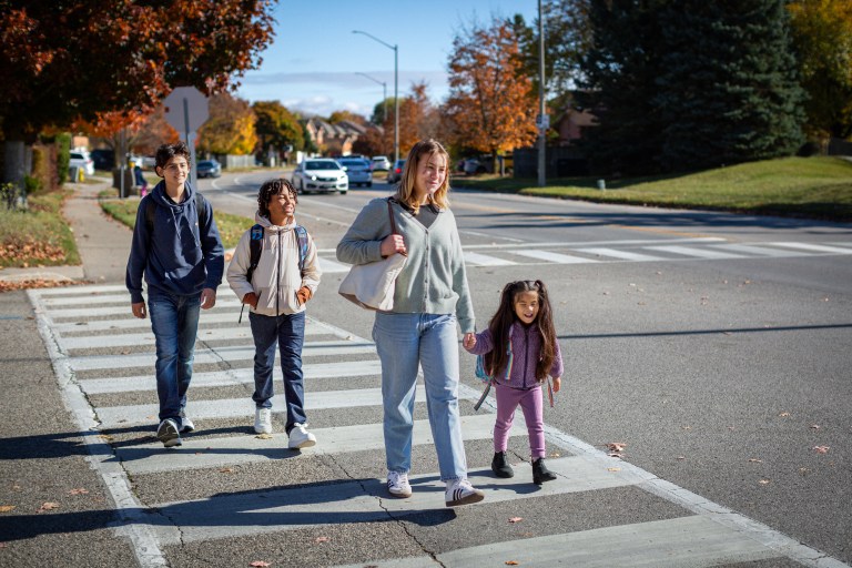 A woman and three children cross the street on a sunny fall day.