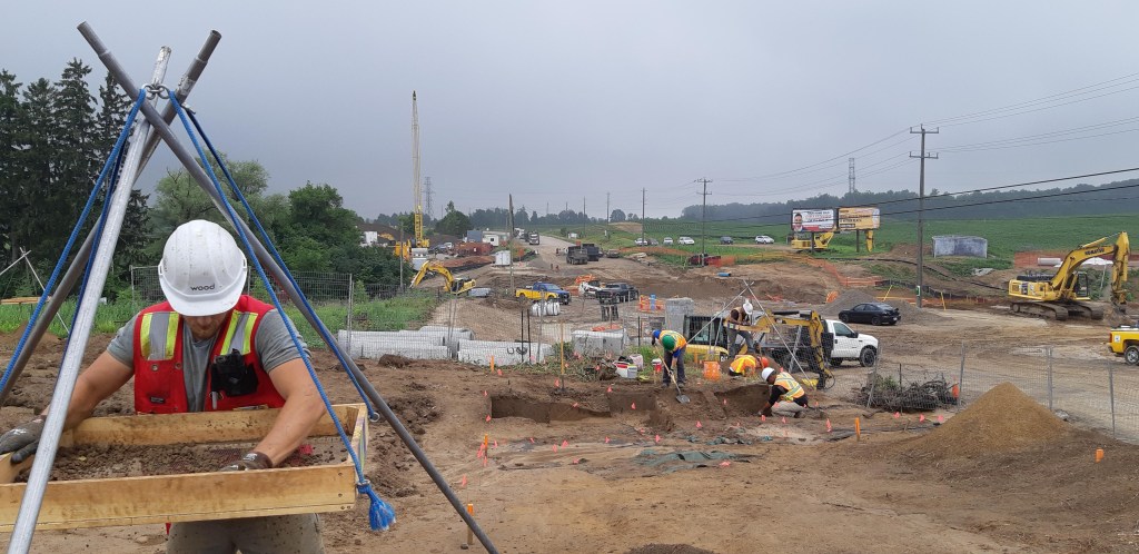 Group of people wearing vests and hard hats work outside.
