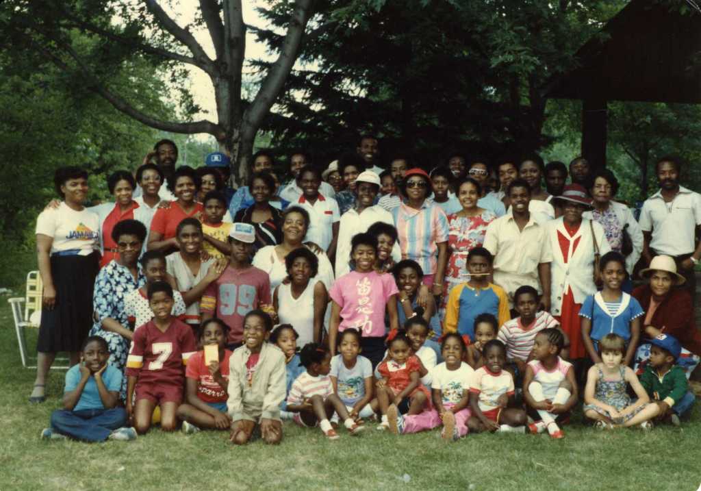 A crowd of adults and children pose outside on the grass.