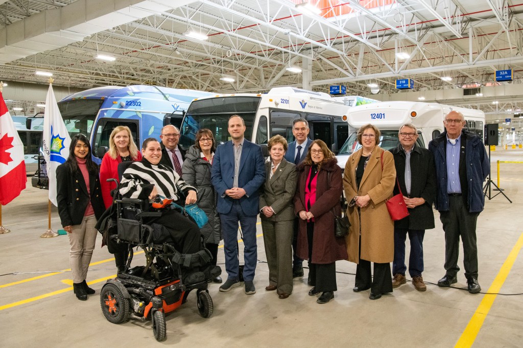 Regional council members and stand in front of buses in a large GRT garage.