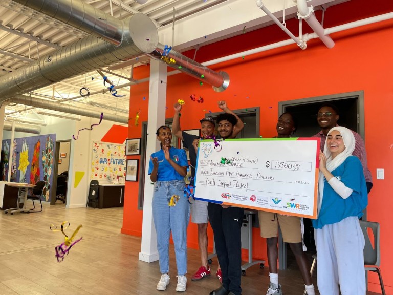 A group of youth hold up a large cheque and cheer.