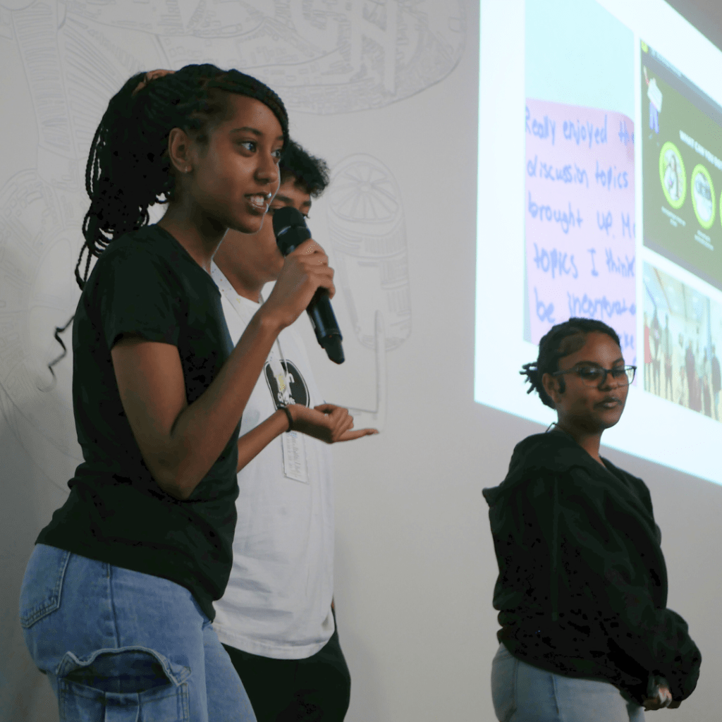 A young woman speaks into a microphone on a stage.