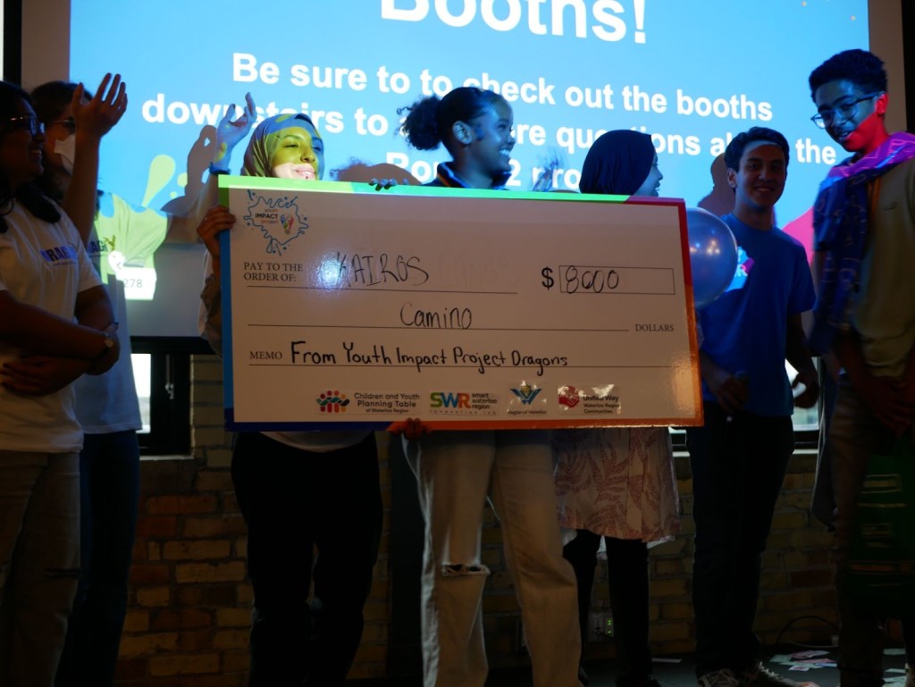 Young people smile while holding a large cheque on a stage.