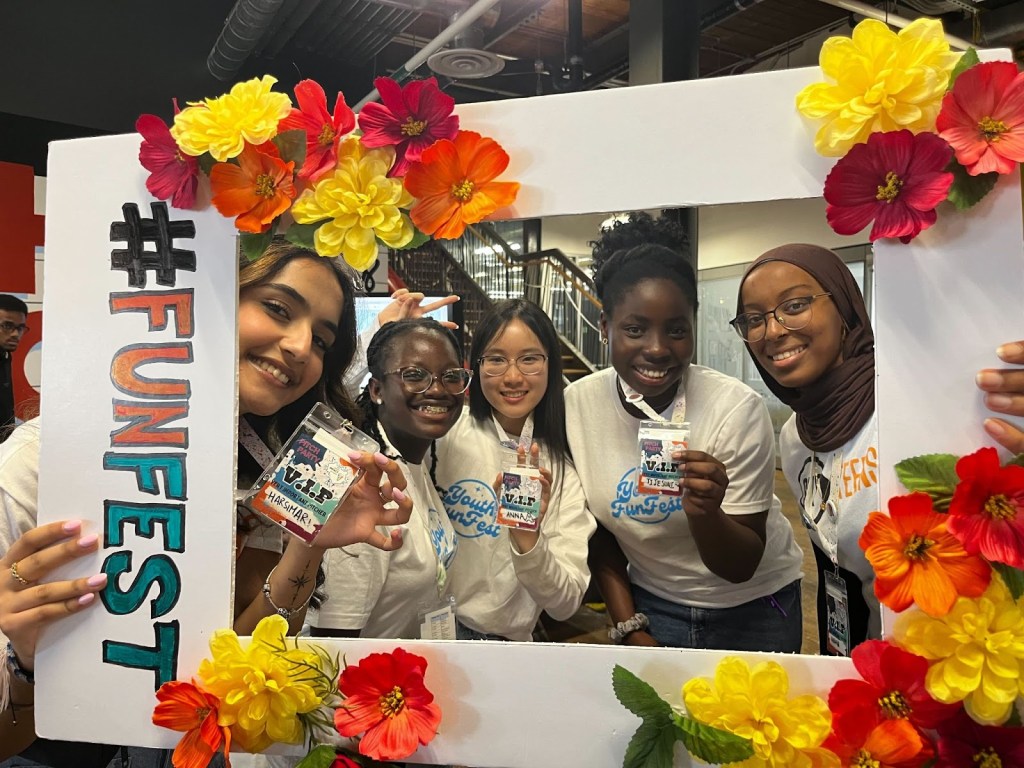 Young people smile behind a flower-covered photo frame.