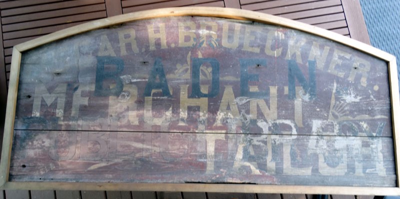 The historic wooden sign as it was found, with faded paint and overlapping words. 