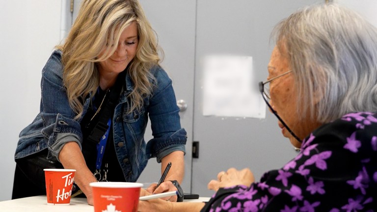 A woman leans over a table with red cups and a white-haired older woman in the foreground.