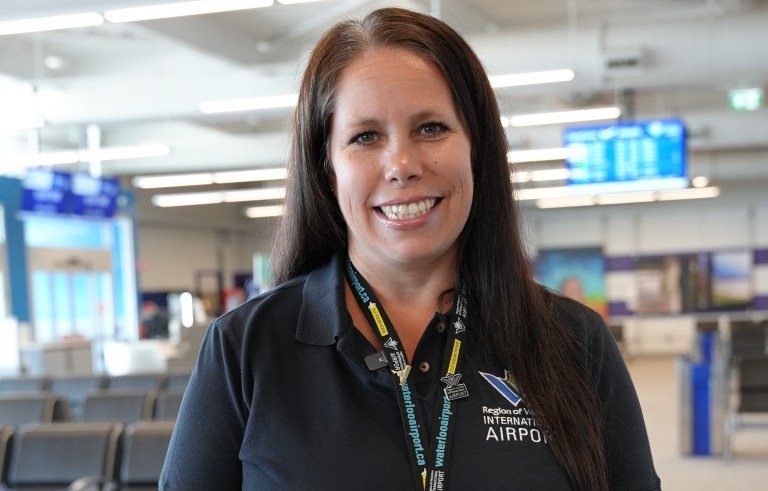 A smiling staff woman standing in the departure lounge area of Region of Waterloo International Airport.
