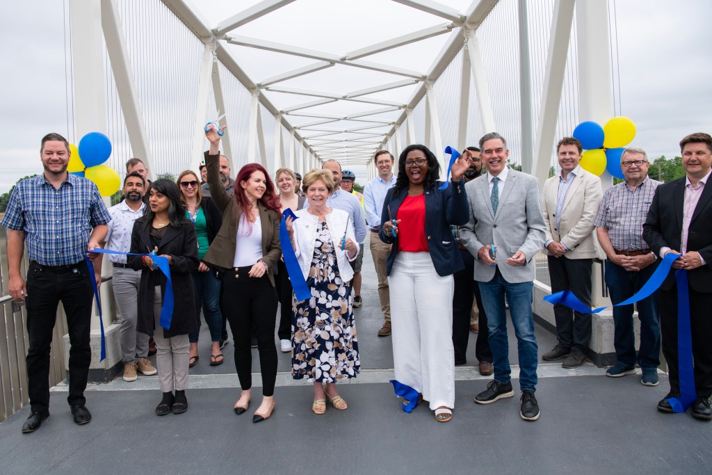 Politicians and officials use scissors to cut a blue ceremonial ribbon at the official opening of a pedestrian bridge in Kitchener.