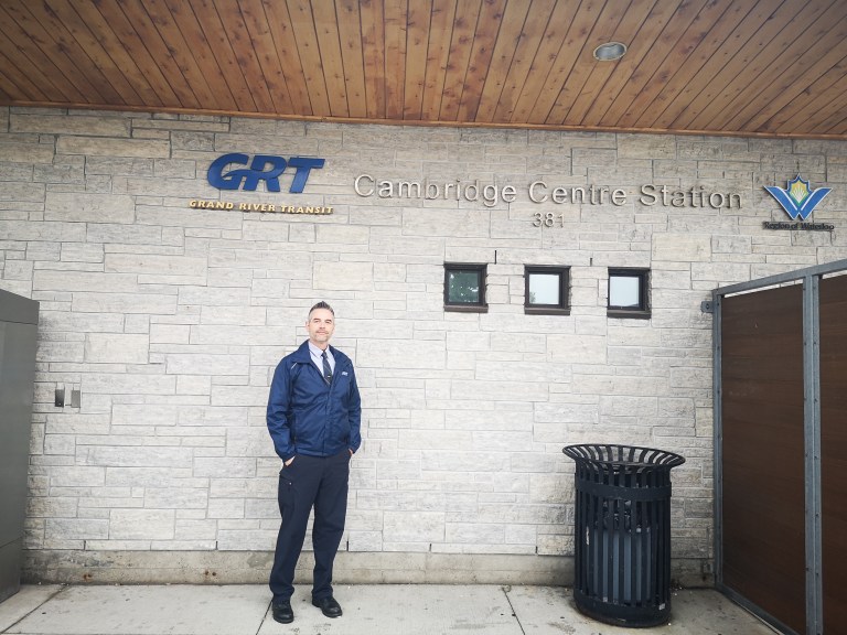 A Grand River Transit bus driver wearing a blue jacket stands in the Cambridge Centre Station.