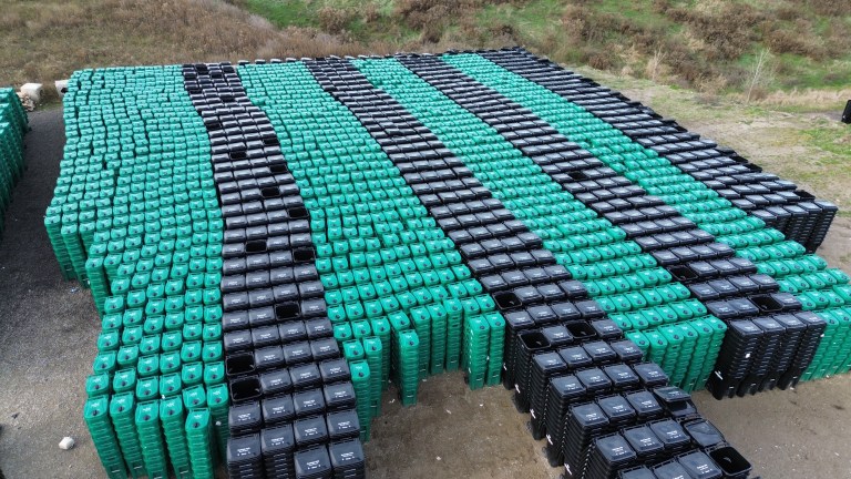 Overhead view of hundreds of new black and green waste carts stacked and ready for delivery.
