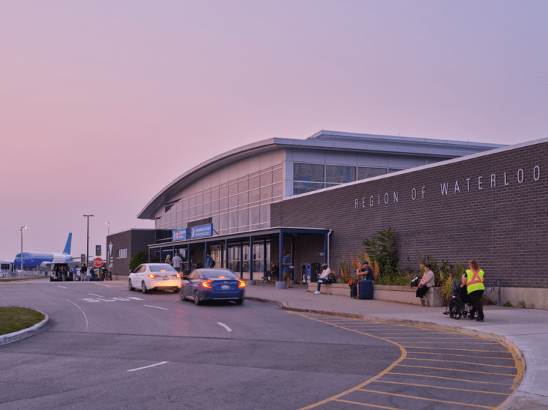 The exterior of Region of Waterloo International Airport, with people arriving on foot, by wheelchair and by car.