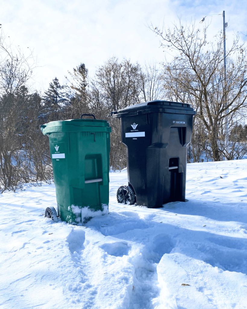 A set of new black and green waste carts sitting in the snow.