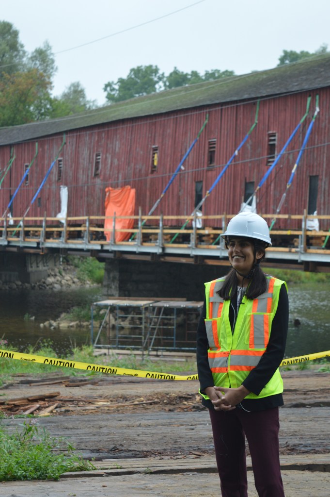 An engineer in high-vis vest and white hard hat stands in front of the West Montrose Bridge.