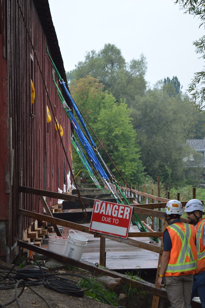Construction workers with high-visibility vests and hard hards work beside the West Montrose Bridge over the Grand River.